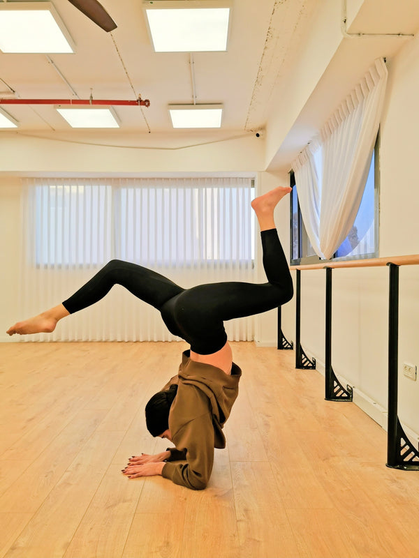 Person doing a handstand in a dance studio with wooden floor and ballet barre. בר כח קבוע מחובר מהרצפה לאימוני פילאטיס, אימוני כח וכושר